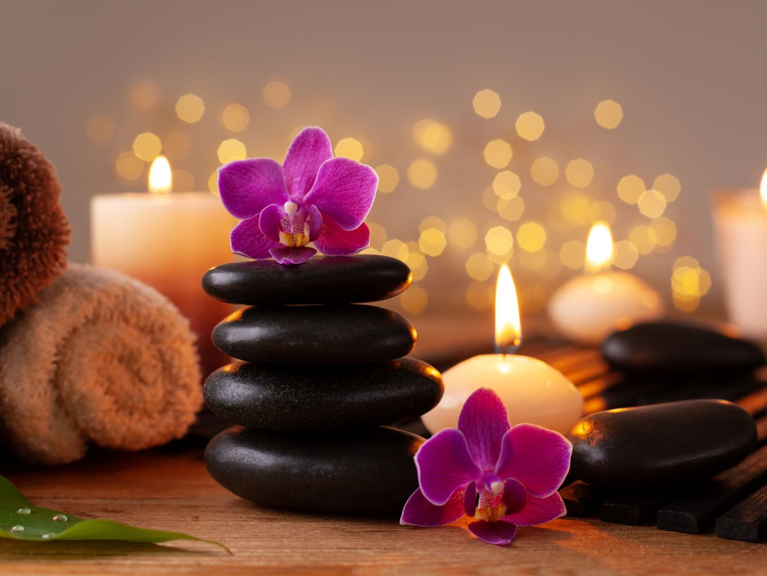 Avslappnande spa-miljö med varma stenar, handdukar och orkidéblommor i ljuslyktors sken hos Suai Massage i Gävle.